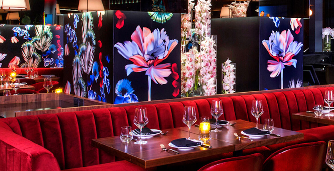 a restaurant with red couches, floral wall decor, and tables