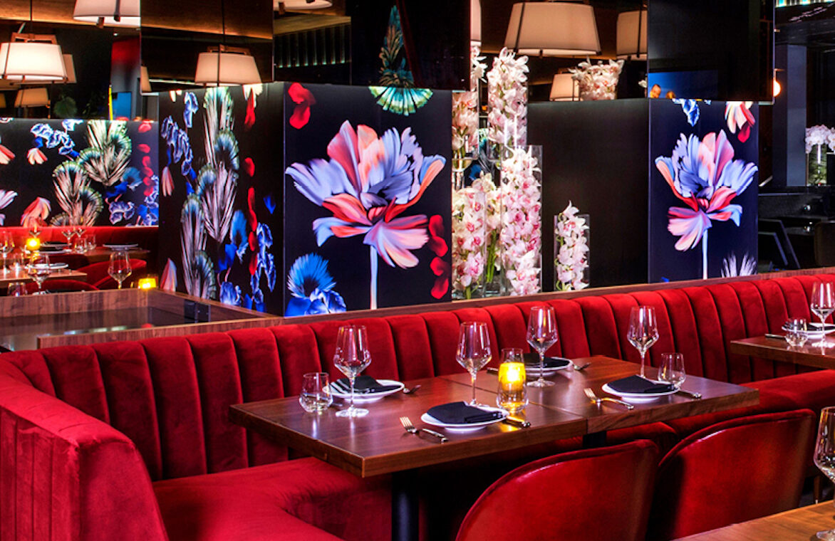 a restaurant with red couches, floral wall decor, and tables