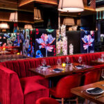 a restaurant with red couches, floral wall decor, and tables